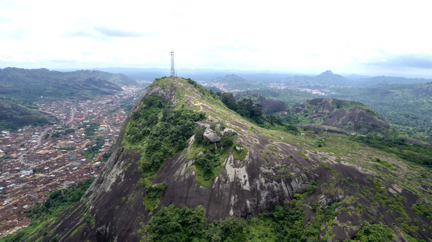 Aerial view of Idanre Hill featuring massive granite rock formations lush green vegetation and a communication tower on the summit overlooking the town of Idanre Ondo State Nigeria. Aerial view of Idanre Hill featuring massive granite rock formations lush green vegetation and a communication tower on the summit overlooking the town of Idanre Ondo State Nigeria.