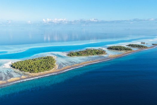 Aerial view of lush tropical islands with green palm trees and turquoise coral reefs surrounded by the deep blue ocean under a clear sky near Vaanee Dhaalu Atoll Maldives. Aerial view of lush tropical islands with green palm trees and turquoise coral reefs surrounded by the deep blue ocean under a clear sky near Vaanee Dhaalu Atoll Maldives.