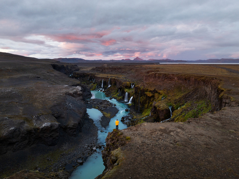 Aerial view of a lone figure in a yellow jacket standing on the precipice of a dramatic canyon carved by a turquoise river Sigöldugljúfur Rangárþing ytra Iceland. Aerial view of a lone figure in a yellow jacket standing on the precipice of a dramatic canyon carved by a turquoise river Sigöldugljúfur Rangárþing ytra Iceland.