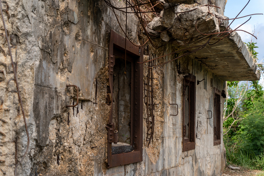 View of the ruins of the North Field Base featuring weathered concrete walls exposed rusted rebar and empty window frames in Northern Tinian Tinian Northern Mariana Islands. View of the ruins of the North Field Base featuring weathered concrete walls exposed rusted rebar and empty window frames in Northern Tinian Tinian Northern Mariana Islands.