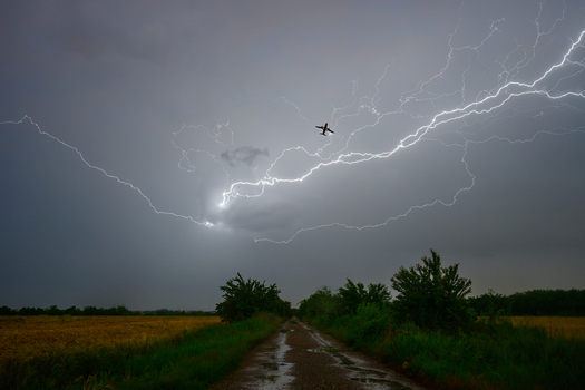 View of a small airplane flying through a dark stormy sky illuminated by a massive lightning bolt above a rural dirt road in Bucharest Bucharest Romania. View of a small airplane flying through a dark stormy sky illuminated by a massive lightning bolt above a rural dirt road in Bucharest Bucharest Romania.