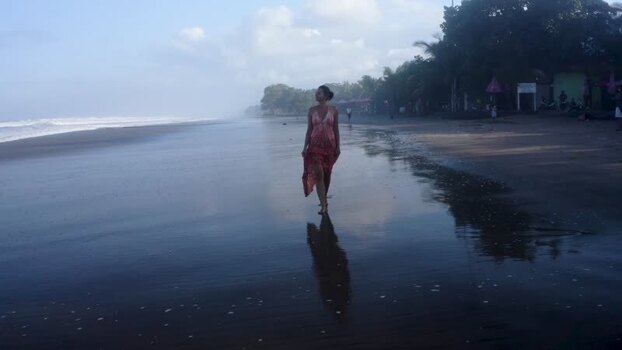 Aerial view of a woman walking on a dark sand beach at sunset Indonesia. Aerial view of a woman walking on a dark sand beach at sunset Indonesia.