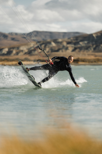 View of a man kitesurfing on the turquoise waters of a lake with mountains in the background in El Chalten Santa Cruz Province Argentina. View of a man kitesurfing on the turquoise waters of a lake with mountains in the background in El Chalten Santa Cruz Province Argentina.