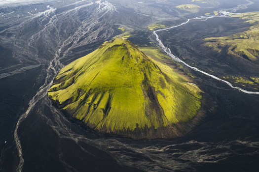 Aerial view of the vibrant green moss covered Maelifell mountain starkly contrasts against the dark volcanic ash plains crisscrossed by glacial rivers Maelifell Iceland. Aerial view of the vibrant green moss covered Maelifell mountain starkly contrasts against the dark volcanic ash plains crisscrossed by glacial rivers Maelifell Iceland.