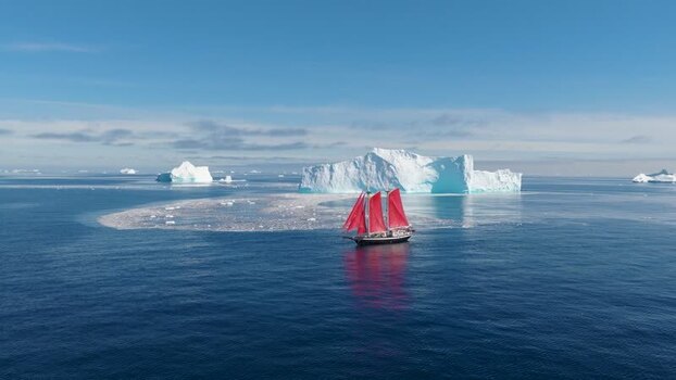 Aerial view of sailboat with red sails near icebergs Greenland. Aerial view of sailboat with red sails near icebergs Greenland.