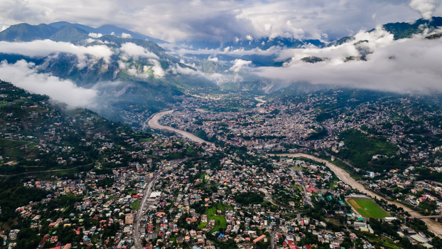 Aerial view of the sprawling city buildings nestled in a deep mountain valley with a winding river under low clouds Muzaffarabad Azad Kashmir Pakistan. Aerial view of the sprawling city buildings nestled in a deep mountain valley with a winding river under low clouds Muzaffarabad Azad Kashmir Pakistan.