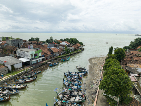 Aerial view of boats docked along the riverbanks with the town s red tiled roofs contrasting against the cloudy sky Jepara Central Java Indonesia.