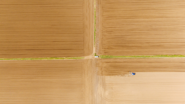 Aerial view of tractors cultivating the land where the earth is a patchwork of browns and tans divided by green lines Sremska Mitrovica Vojvodina Serbia. Aerial view of tractors cultivating the land where the earth is a patchwork of browns and tans divided by green lines Sremska Mitrovica Vojvodina Serbia.