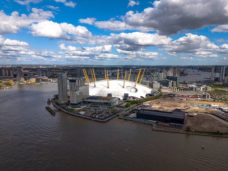 Aerial view of The O2 arena on the Greenwich Peninsula surrounded by the River Thames and modern skyscrapers under a cloudy sky London England United Kingdom.