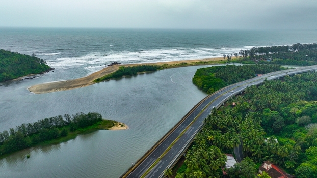 Aerial view of Galgibaga Beach where the river meets the Arabian Sea with a bridge crossing the water surrounded by palm trees and coastal vegetation in Canacona Goa India.