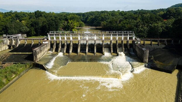 Aerial view of Jalaur Dam with water flowing through the spillway surrounded by lush green forest and vegetation in Dingle Western Visayas Philippines.