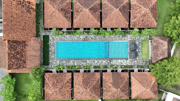 Aerial view of a rectangular blue swimming pool surrounded by stone paving and traditional terracotta roofed villas in Borobudur Central Java Indonesia. Aerial view of a rectangular blue swimming pool surrounded by stone paving and traditional terracotta roofed villas in Borobudur Central Java Indonesia.