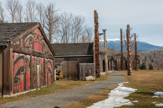 View of the traditional wooden longhouses with intricate red and black carvings and tall totem poles at Ksan Historical Village in Ksan British Columbia Canada. View of the traditional wooden longhouses with intricate red and black carvings and tall totem poles at Ksan Historical Village in Ksan British Columbia Canada.