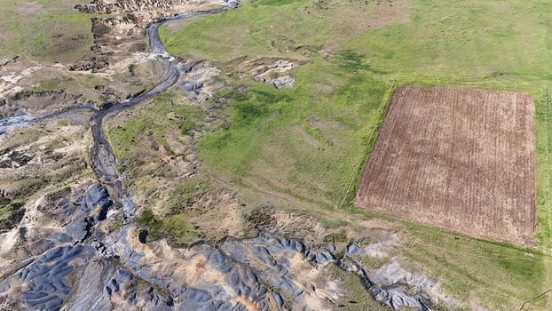 Aerial view of severe soil erosion and a dry riverbed next to a rectangular ploughed field in the rural landscape of Pietermaritzburg KwaZulu Natal South Africa.