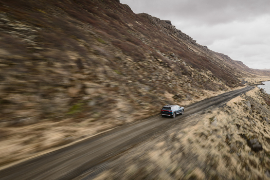 Aerial view of a car driving on a coastal road beside Hlidarvatn lake surrounded by rugged rocky hills under an overcast sky in Sveitarfelagid Olfus Iceland. Aerial view of a car driving on a coastal road beside Hlidarvatn lake surrounded by rugged rocky hills under an overcast sky in Sveitarfelagid Olfus Iceland.