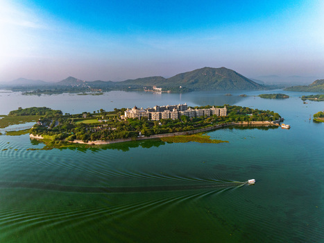Aerial view of the Taj Lake Palace surrounded by the calm waters of Lake Pichola with lush greenery and distant hills in Udaipur Rajasthan India. Aerial view of the Taj Lake Palace surrounded by the calm waters of Lake Pichola with lush greenery and distant hills in Udaipur Rajasthan India.