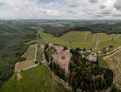 Aerial view of the historic Badia di Passignano abbey surrounded by lush vineyards cypress trees and rolling hills in Passignano Toscana Italy.