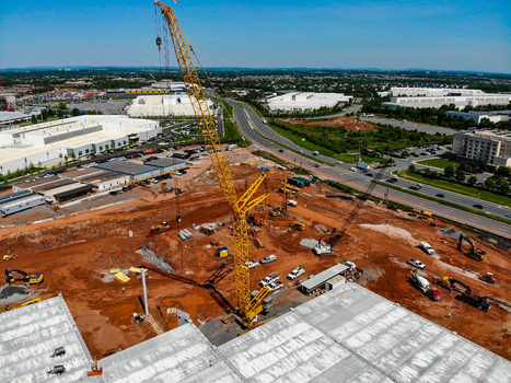 Aerial view of a large yellow crane at a construction site with heavy machinery and red earth surrounded by industrial buildings and roads in Ashburn Virginia United States. Aerial view of a large yellow crane at a construction site with heavy machinery and red earth surrounded by industrial buildings and roads in Ashburn Virginia United States.