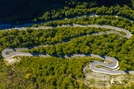 Aerial view of a winding mountain road with sharp hairpin turns cutting through a dense green forest in the hills Skofja Loka Slovenia.