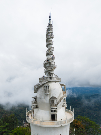 Aerial view of Ambuluwawa Tower with its unique spiral staircase and people climbing surrounded by misty mountains and lush greenery in Gampola Central Province Sri Lanka. Aerial view of Ambuluwawa Tower with its unique spiral staircase and people climbing surrounded by misty mountains and lush greenery in Gampola Central Province Sri Lanka.