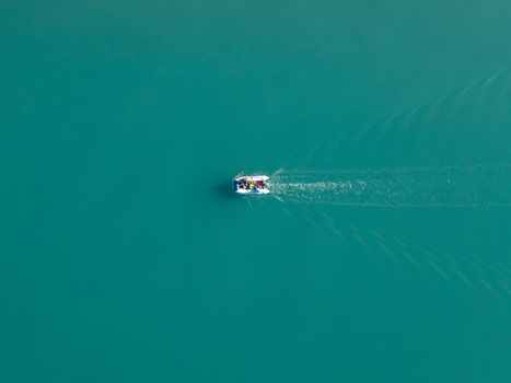 Aerial view of a small boat with people moving across the turquoise waters of Kanali i Vivarit leaving a white wake behind Vrine Vlore County Albania. Aerial view of a small boat with people moving across the turquoise waters of Kanali i Vivarit leaving a white wake behind Vrine Vlore County Albania.