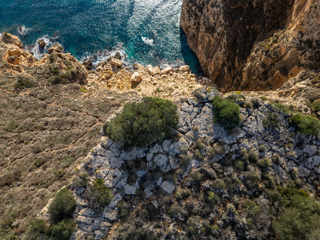 Aerial view of the rugged cliffs and rocky coastline of Cala Llebeig with Mediterranean vegetation and turquoise waters in El Poble Nou de Benitatxell Valencian Community Spain.