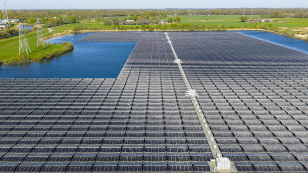 Aerial view of a massive floating solar farm on a calm lake surrounded by green fields and power lines in Zwolle Overijssel Netherlands. Aerial view of a massive floating solar farm on a calm lake surrounded by green fields and power lines in Zwolle Overijssel Netherlands.