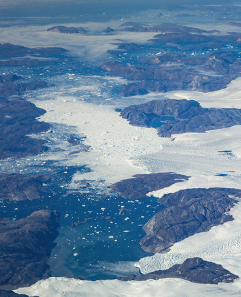 Aerial view of a glacial river dotted with icebergs flows through rugged rocky terrain contrasting with the vast white expanse of ice Narsarsuaq Greenland.