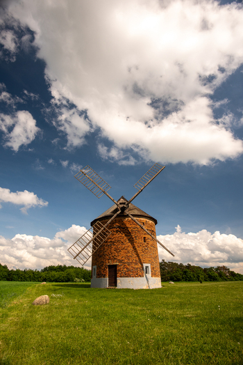 View of a historic brick windmill standing in a green field under a bright blue sky with fluffy white clouds in Brno City District South Moravian Region Czechia.
