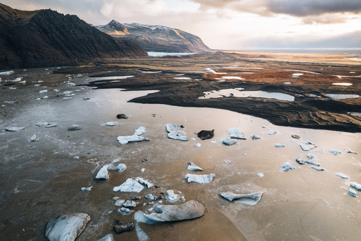 Aerial view of the Skaftafell glacial lagoon with floating icebergs dark volcanic plains and mountains at sunset in Skaftafell Sveitarfelagid Hornafjordur Iceland. Aerial view of the Skaftafell glacial lagoon with floating icebergs dark volcanic plains and mountains at sunset in Skaftafell Sveitarfelagid Hornafjordur Iceland.