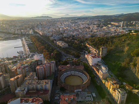Aerial view of Plaza de toros de La Malagueta bullring surrounded by urban buildings the port area and distant mountains under a soft sky in Malaga Andalusia Spain. Aerial view of Plaza de toros de La Malagueta bullring surrounded by urban buildings the port area and distant mountains under a soft sky in Malaga Andalusia Spain.
