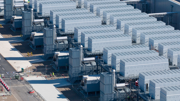 Aerial view of Datacenter Westpoort featuring rows of industrial cooling units and metal infrastructure with a worker on site in Groningen Groningen Netherlands. Aerial view of Datacenter Westpoort featuring rows of industrial cooling units and metal infrastructure with a worker on site in Groningen Groningen Netherlands.