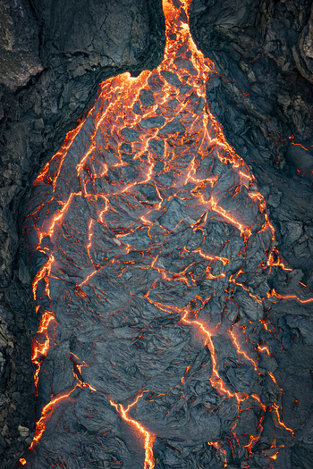 Aerial view of molten lava cascading down dark volcanic rock a fiery river against a stark contrasting landscape Grindav&iacute;kurb&aelig;r Iceland.