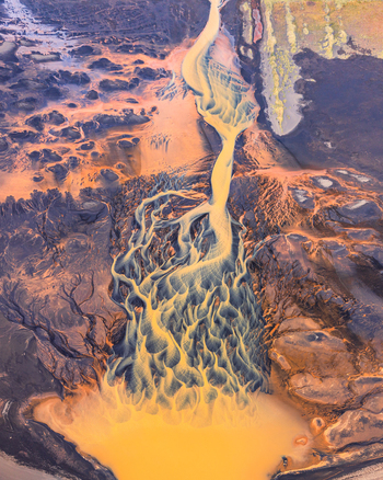 Aerial view of a golden hued braided glacial river flowing through a dark volcanic landscape in Iceland. Aerial view of a golden hued braided glacial river flowing through a dark volcanic landscape in Iceland.