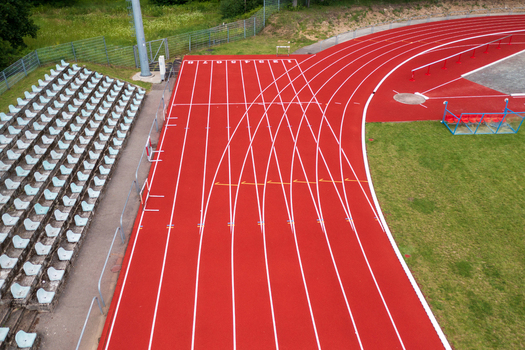 Aerial view of a red running track with white lane markings and empty stadium seating next to a green field Vilnius County Lithuania. Aerial view of a red running track with white lane markings and empty stadium seating next to a green field Vilnius County Lithuania.