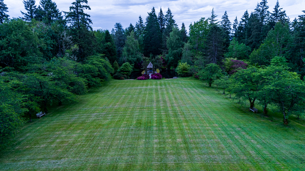 Aerial view of a large manicured lawn with mowed patterns surrounded by a lush green forest and a small garden pavilion in Portland Oregon United States. Aerial view of a large manicured lawn with mowed patterns surrounded by a lush green forest and a small garden pavilion in Portland Oregon United States.