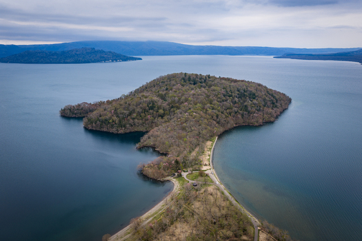 Aerial view of Nakajima island in the center of Lake Kussharo surrounded by deep blue water lush forest and a sandy shoreline under a cloudy sky in Teshikaga Hokkaido Japan. Aerial view of Nakajima island in the center of Lake Kussharo surrounded by deep blue water lush forest and a sandy shoreline under a cloudy sky in Teshikaga Hokkaido Japan.
