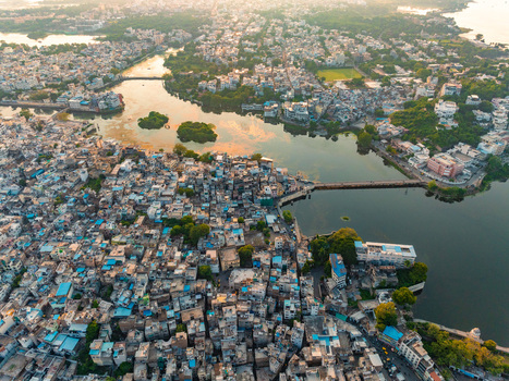 Aerial view of the historic city of Udaipur with dense urban architecture winding streets and the serene waters of Lake Pichola reflecting the warm sunset light in Udaipur Rajasthan India.