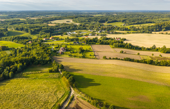Aerial view of the Kashubia region featuring rolling green meadows agricultural fields dense forests and scattered rural houses under a clear sky. Pomeranian Voivodeship Poland. Aerial view of the Kashubia region featuring rolling green meadows agricultural fields dense forests and scattered rural houses under a clear sky. Pomeranian Voivodeship Poland.