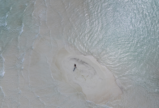 Aerial view of a person standing on a small isolated sandbank surrounded by clear shallow turquoise water in the Maldives. Aerial view of a person standing on a small isolated sandbank surrounded by clear shallow turquoise water in the Maldives.