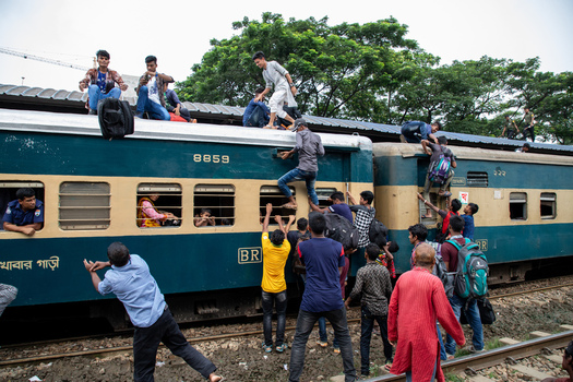 Dhaka Bangladesh 14 June 2018 View of people climbing onto an overcrowded train at Airport Railway Station with passengers on the roof and hanging from windows. Dhaka Bangladesh 14 June 2018 View of people climbing onto an overcrowded train at Airport Railway Station with passengers on the roof and hanging from windows.