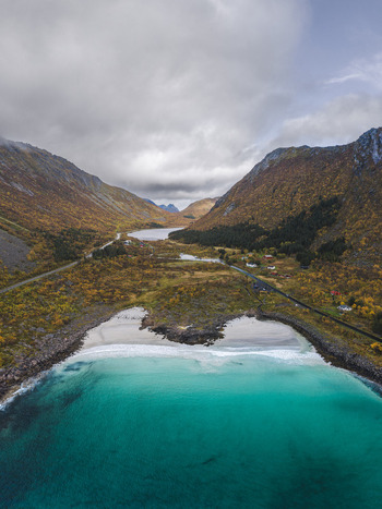 Aerial view of Lofoten beach with turquoise water surrounded by dramatic mountains with autumn foliage and a coastal road in Leknes Nordland Norway. Aerial view of Lofoten beach with turquoise water surrounded by dramatic mountains with autumn foliage and a coastal road in Leknes Nordland Norway.
