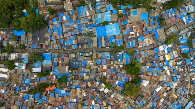 Aerial view of Dharavi Slums in Mumbai showing dense clusters of small houses with blue tarpaulin roofs narrow alleyways and scattered trees Mumbai Maharashtra India. Aerial view of Dharavi Slums in Mumbai showing dense clusters of small houses with blue tarpaulin roofs narrow alleyways and scattered trees Mumbai Maharashtra India.