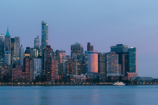 View of the New York City skyline at dusk with illuminated skyscrapers reflecting golden light seen across the East River New York New York United States.