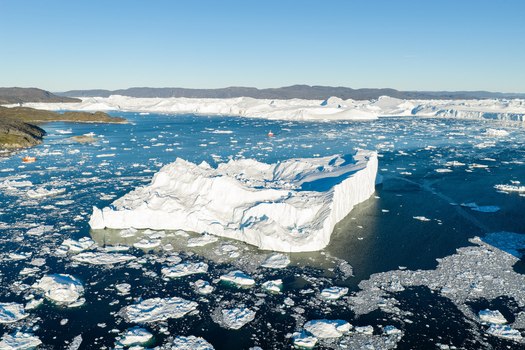 Aerial view of a massive iceberg floating in the Ilulissat Icefjord surrounded by scattered ice fragments and deep blue water with rocky coastlines Greenland. Aerial view of a massive iceberg floating in the Ilulissat Icefjord surrounded by scattered ice fragments and deep blue water with rocky coastlines Greenland.