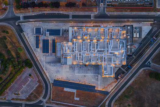 Aerial view of a modern datacenter facility featuring complex rooftop HVAC systems solar panel arrays and surrounding paved parking areas in Settecamini Lazio Italy.
