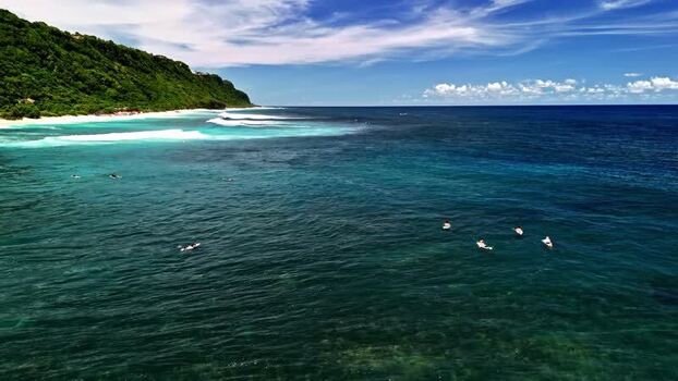 Aerial view of surfers in the turquoise ocean near Bali Indonesia.