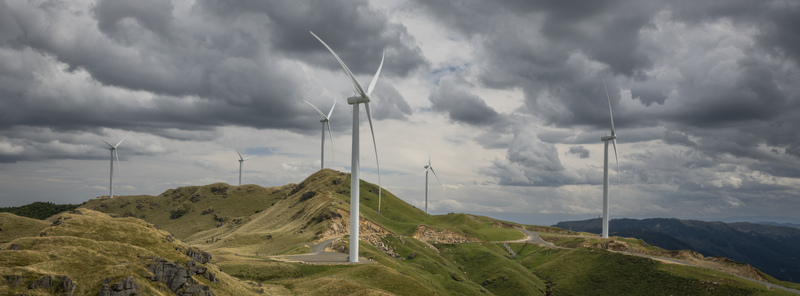 View of Harapaki Wind Farm with white wind turbines standing on rolling green hills under a dramatic cloudy sky in Te Haroto Hawke s Bay Region New Zealand. View of Harapaki Wind Farm with white wind turbines standing on rolling green hills under a dramatic cloudy sky in Te Haroto Hawke s Bay Region New Zealand.