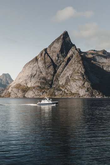 Sund Nordland Norway 08 September 2022 View of a small boat navigating the calm waters of a fjord beneath towering rugged mountain peaks under a clear sky.