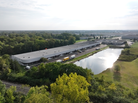 Aerial view of a long industrial warehouse building with a parking lot trucks and a small pond surrounded by trees in Indianapolis Indiana United States. Aerial view of a long industrial warehouse building with a parking lot trucks and a small pond surrounded by trees in Indianapolis Indiana United States.